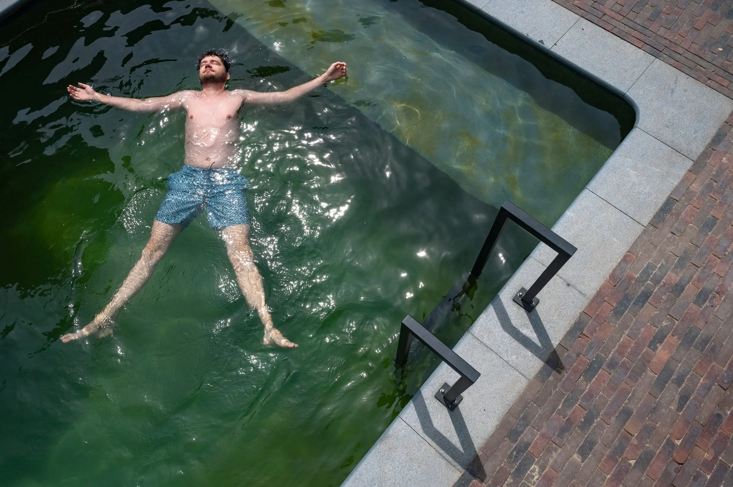 Iemand drijft op de rug in het heldere, groene water van het ecologisch zwembad, van bovenaf gezien