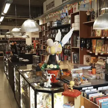 Winkelinterieur met een groot Asterix-beeld tussen toonbanken vol strips en gezelschapsspellen