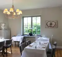 Eetzaal met witgedekte tafels, een luchter en uitzicht op de tuin