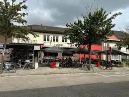 De gevel van het eetcafé met een straatterras onder rode parasols en fietsen ervoor