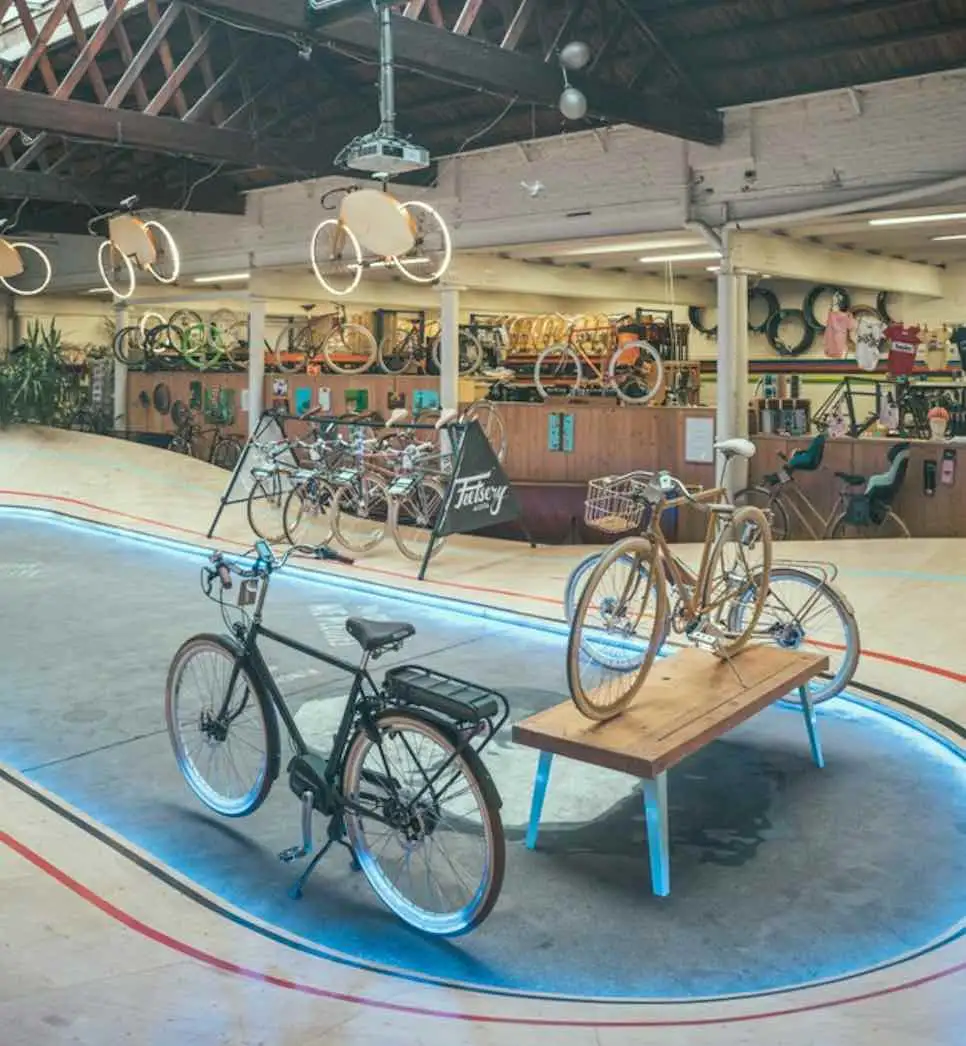 Fietsen in een hoge industriële hal met een houten wielerbaan en een bord van de fietsenwinkel