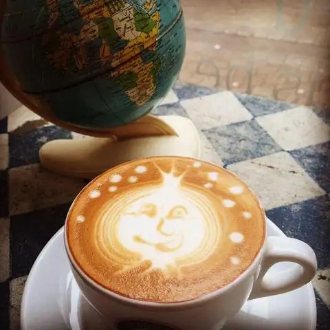 Cappuccino met latte art in de vorm van een lachend zonnetje, naast een wereldbol